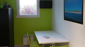 Una habitación pequeña con una mesa, una silla, una ventana que da a árboles y un televisor en la pared.