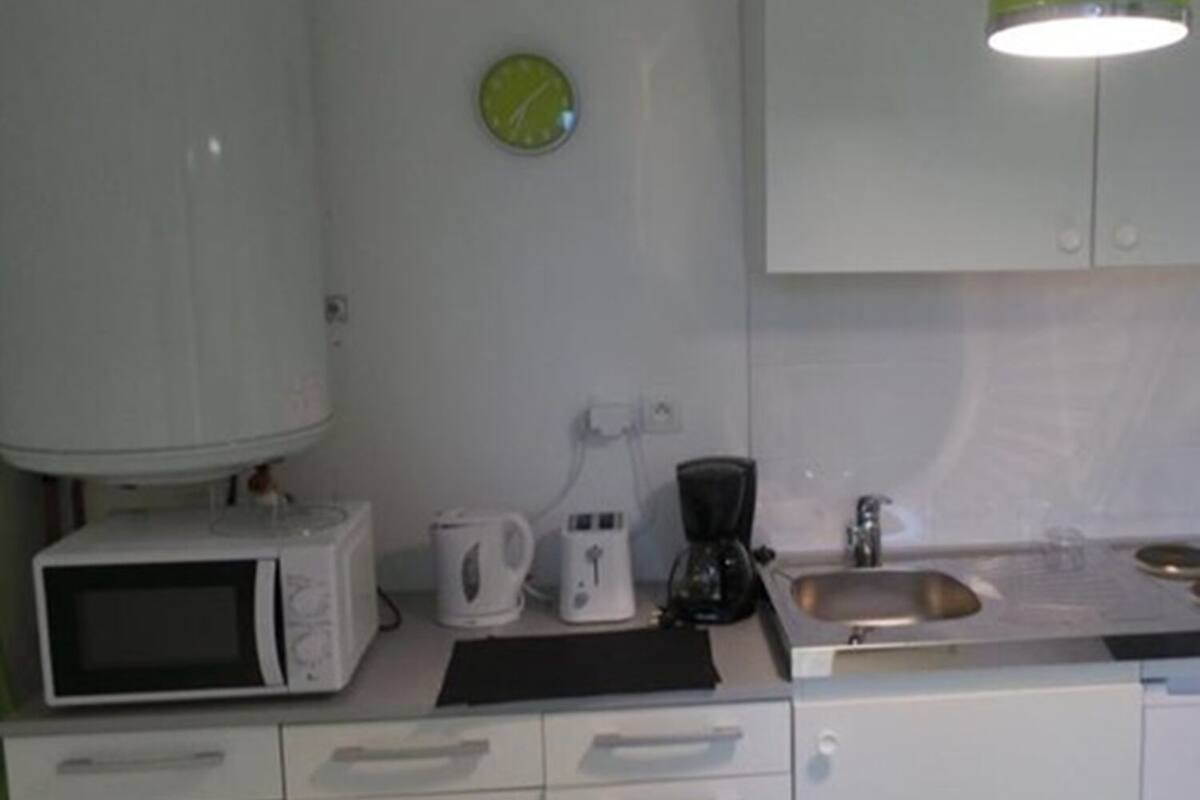 A kitchen with white cabinets, a microwave, a coffee maker, a sink, and a green clock on the wall.