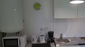 Una cocina con armarios blancos, un microondas, una cafetera, un lavamanos y un reloj verde en la pared.
