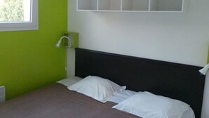 Una cama individual con ropa de cama blanca en una habitación con paredes verdes y un cabecero blanco.