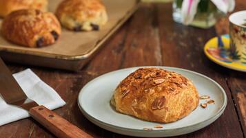 A rustic wooden table with a plate of croissants, a knife, and a pastry tray in the background.