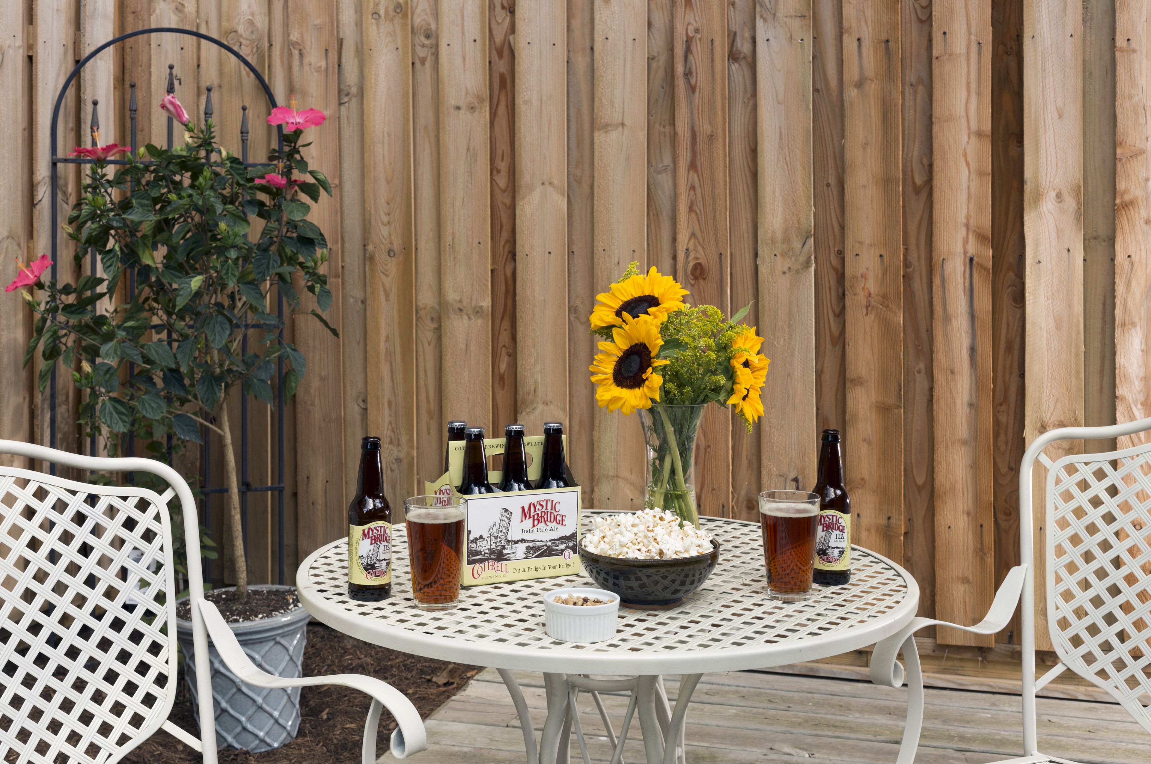A round table with a beer box, bottles, a bowl of popcorn, and a glass of beer.