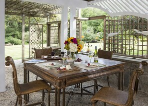 A covered patio with a wooden table set for dining, surrounded by wicker chairs. - Abbey's Lantern Hill Inn (Ledyard)