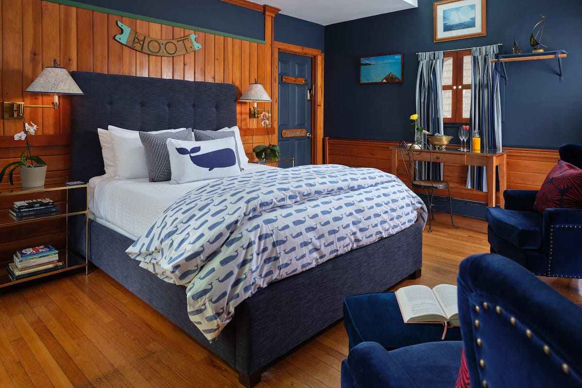 A neatly arranged bedroom with a bed, bedside tables, a reading chair, and a desk.