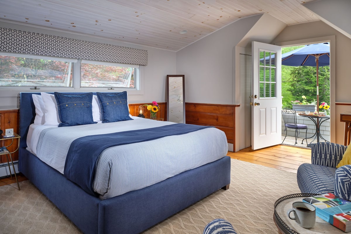 A bedroom with a large bed, a bedside table, a chair, a coffee table, and a view of the outdoors.
