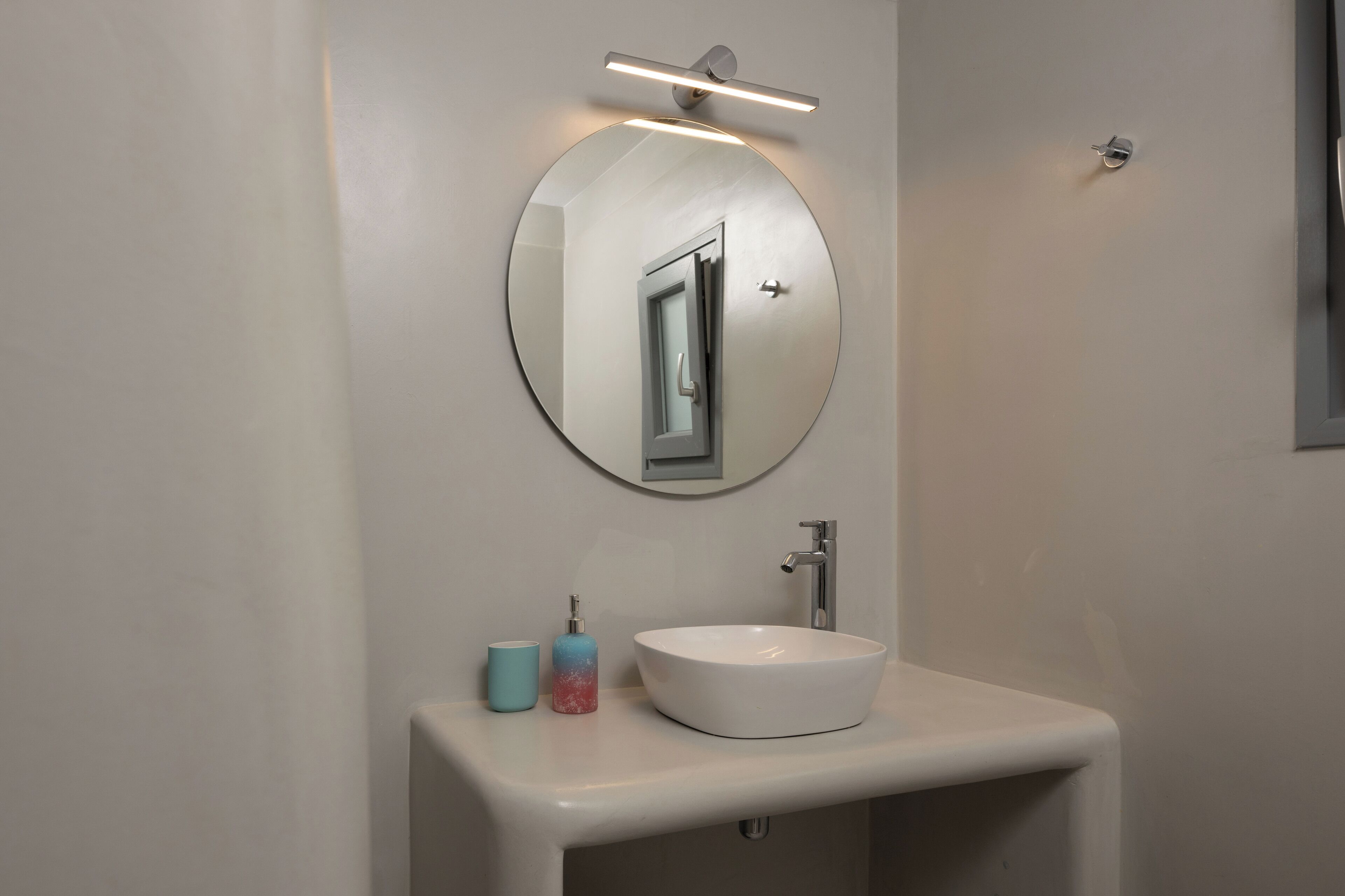 A bathroom with a round mirror, a white sink, and a soap dispenser.