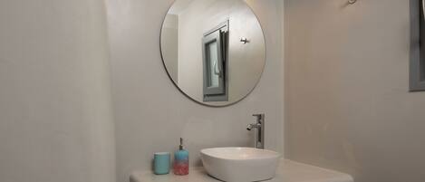 A bathroom with a round mirror, a white sink, and a soap dispenser.