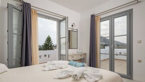 Et hotelværelse med seng, kommode, spejl og en balkon med udsigt over byen.