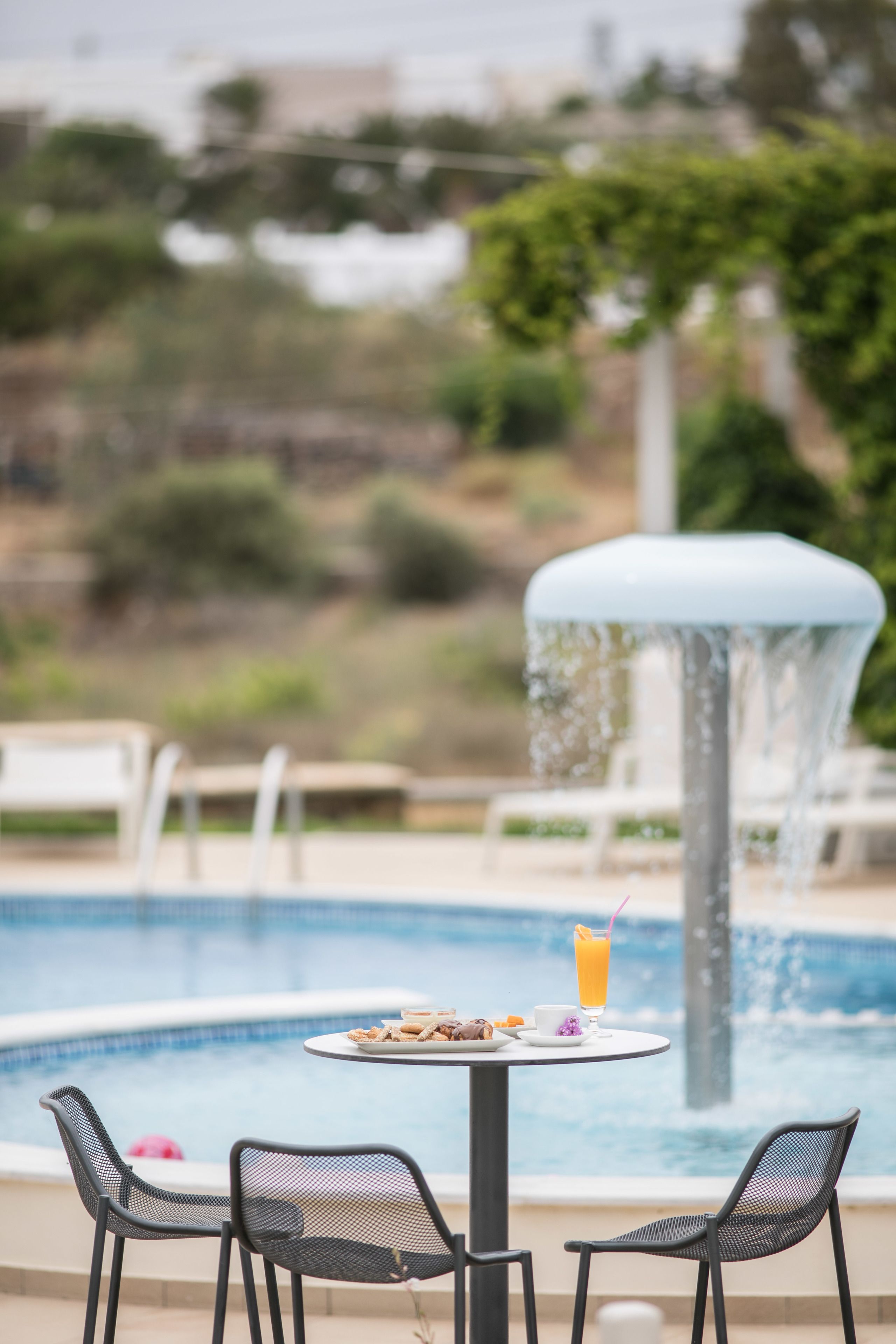Un espace repas aménagé au bord de la piscine, avec une table et des chaises, une fontaine et une vue sur la piscine.