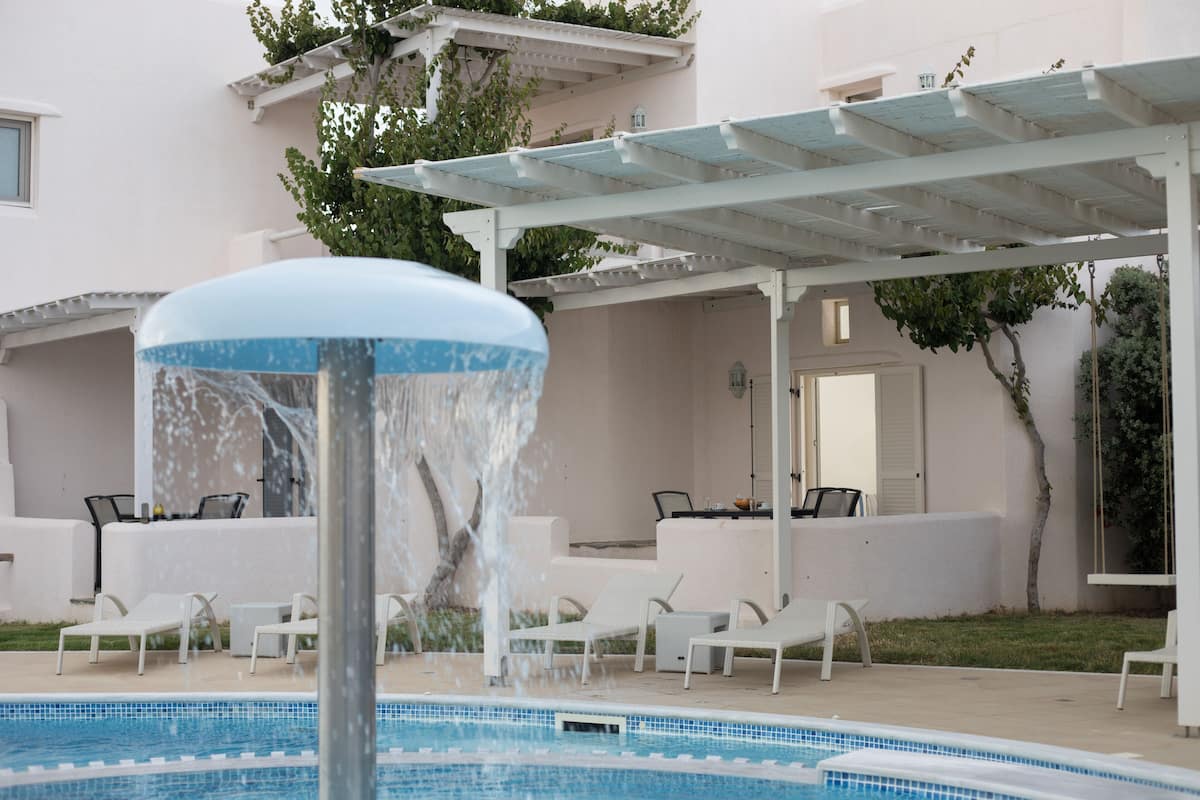 Een zwembadgedeelte met een waterpartij, ligbedden en een pergola.