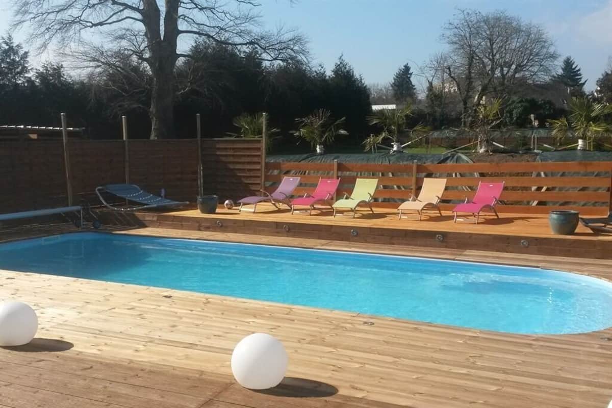 Une piscine entourée d’une terrasse en bois et agrémentée de chaises longues colorées.