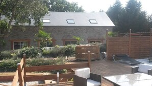 A wooden deck with outdoor seating, a swimming pool, and a stone building with windows.