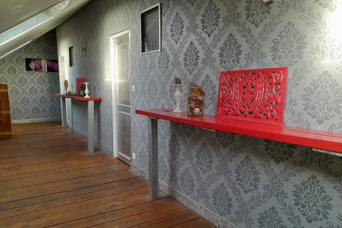 Un couloir avec un papier peint à motifs, un plancher en bois et des étagères rouges sur lesquelles sont disposés divers objets.