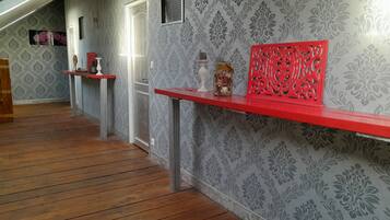 A hallway with patterned wallpaper, wooden flooring, and red shelves with various items.