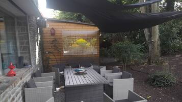 Relax in the serene garden setting, surrounded by lush greenery and a shaded patio with a wooden table and six comfortable chairs.