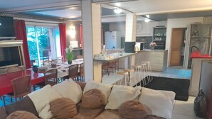 A living room with a sectional sofa, a dining area with a table and chairs, and a kitchen area with a refrigerator and bar stools. - Le Domaine de la Belle Normandie (Condé-en-Normandie)