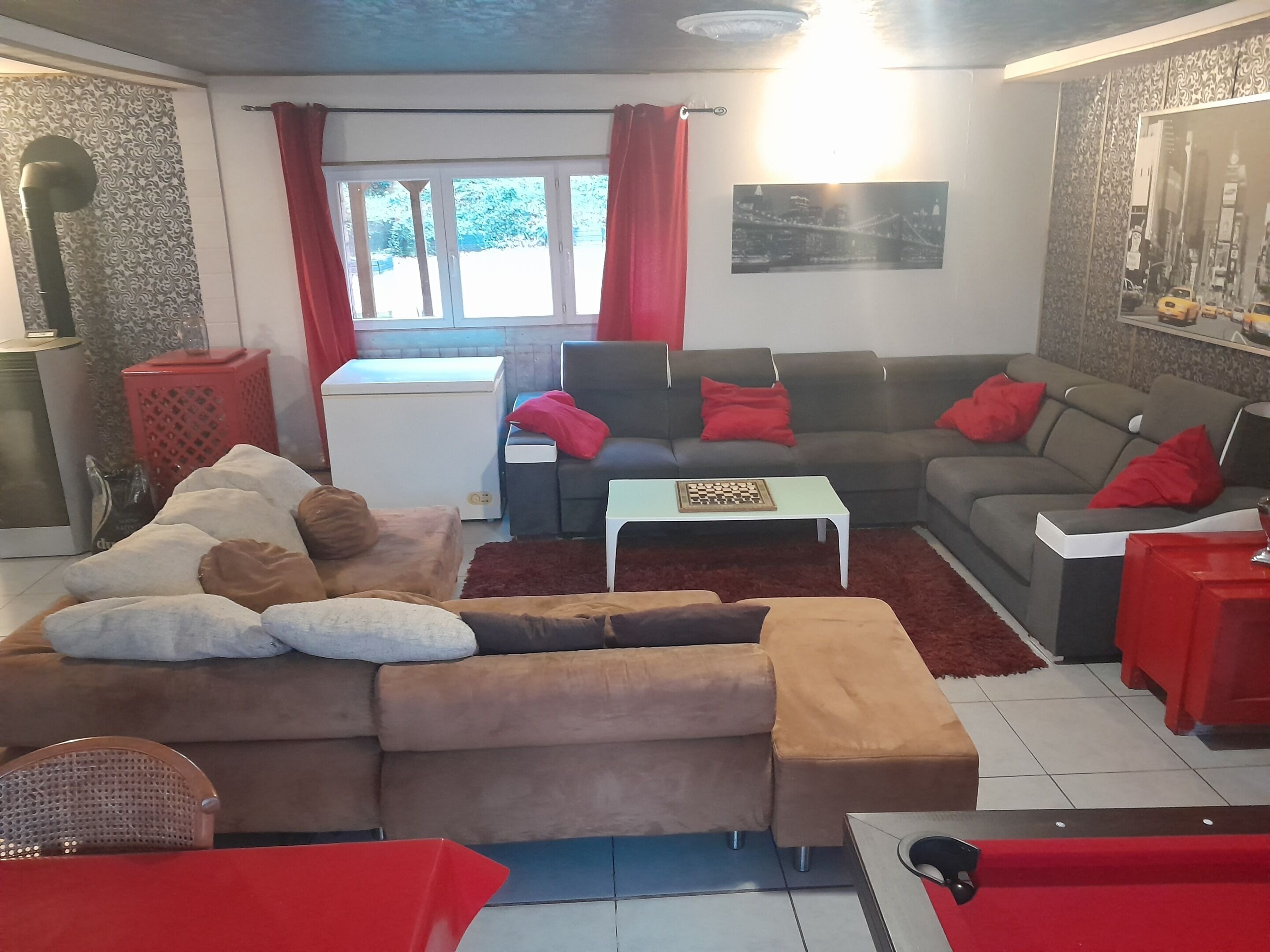 Un saló amb un sofà, una taula de centre i una cadira vermella. Hi ha una finestra amb cortines, un radiador i un quadre penjat a la paret.