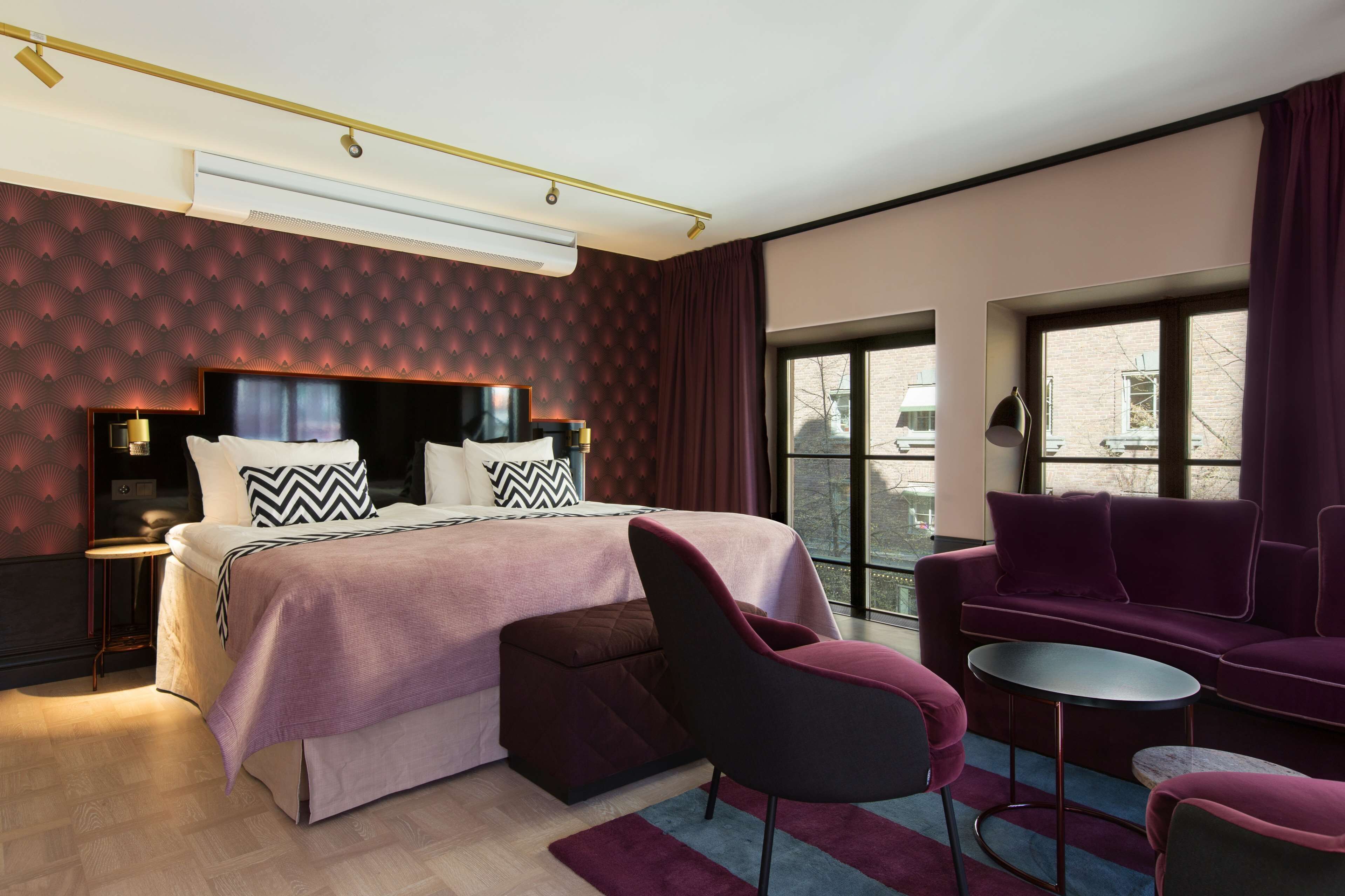 Une chambre d’hôtel moderne, dotée d’un grand lit, d’un canapé, d’une petite table et offrant une vue sur l’extérieur grâce à de grandes fenêtres.