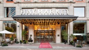 La entrada del hotel Haymarket con alfombra roja, asientos exteriores y luces colgantes.