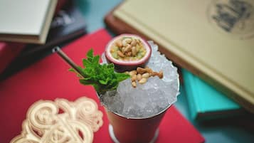 Cóctel con hielo y una rodaja de maracuyá, adornado con nueces, sobre una superficie roja con libros y un objeto decorativo cerca.
