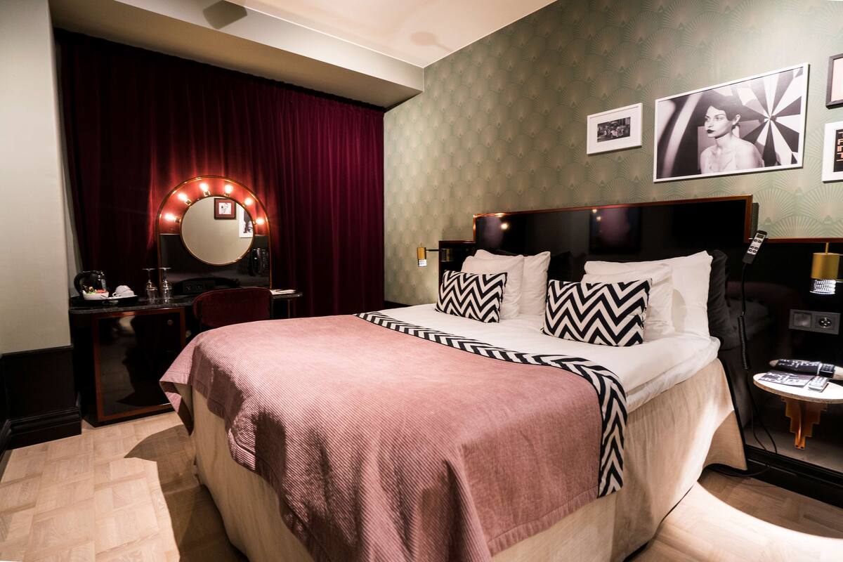 Une chambre d’hôtel avec un grand lit, une coiffeuse avec un miroir, un bureau et une chaise.