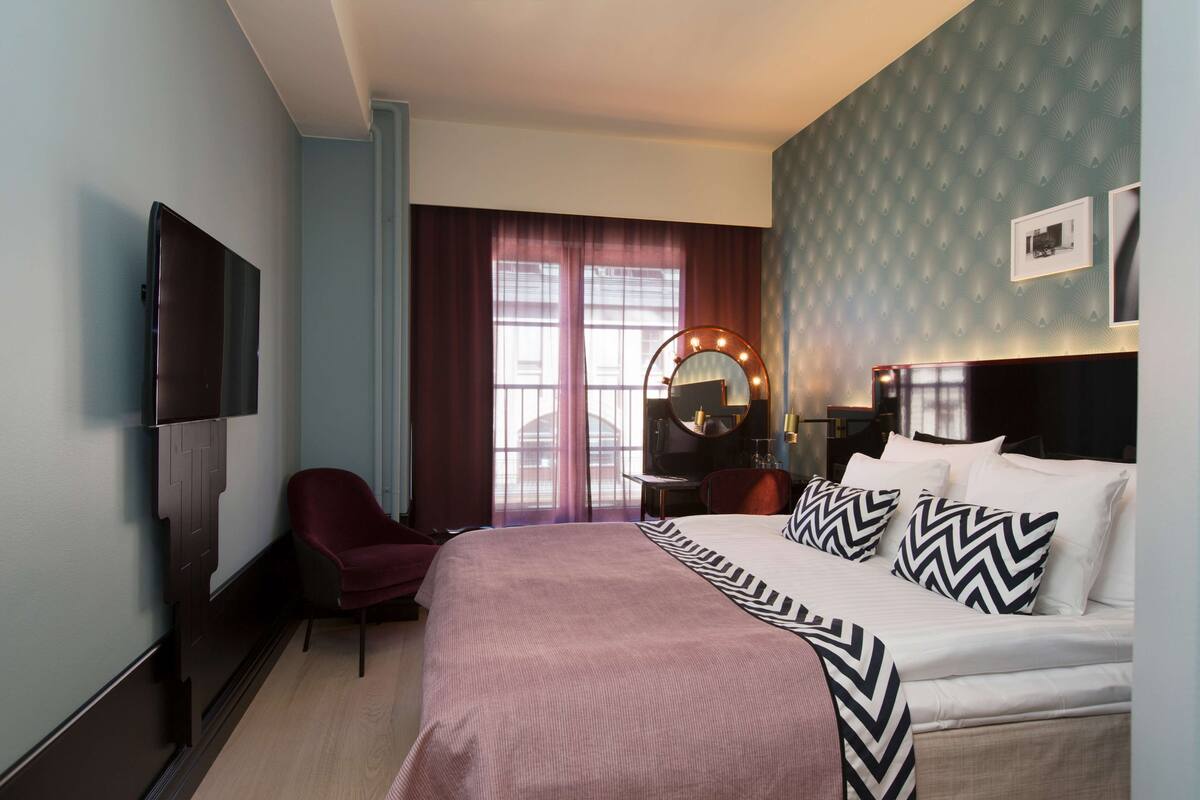 Une chambre d’hôtel avec un grand lit, une coiffeuse avec un miroir, une chaise et un téléviseur fixé au mur.