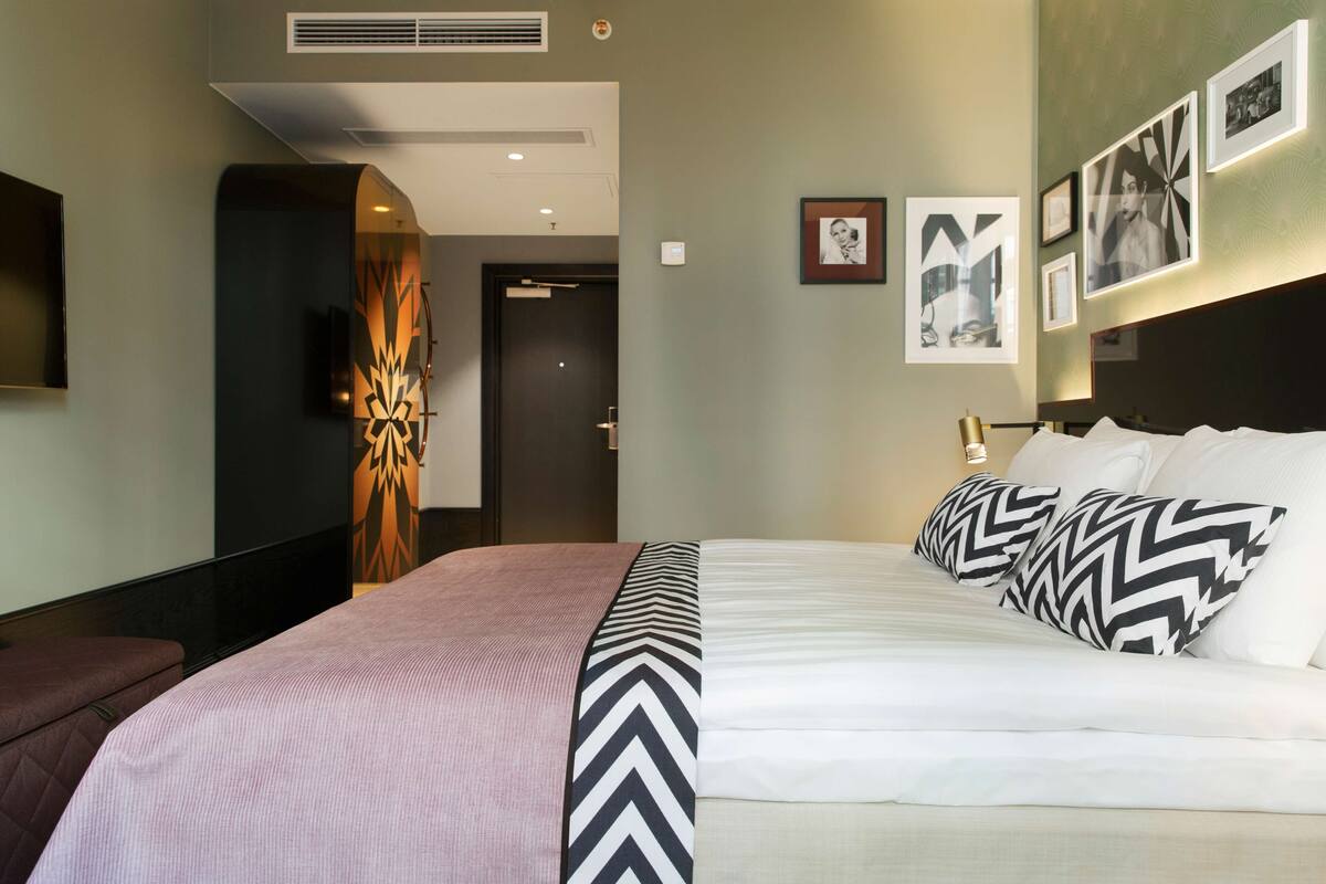 Une chambre d’hôtel avec un grand lit, un téléviseur fixé au mur et des tableaux encadrés accrochés au mur.