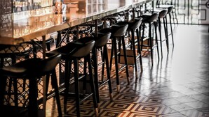 Een bar met een lange toonbank, meerdere barkrukken en hangende pendantlampen.