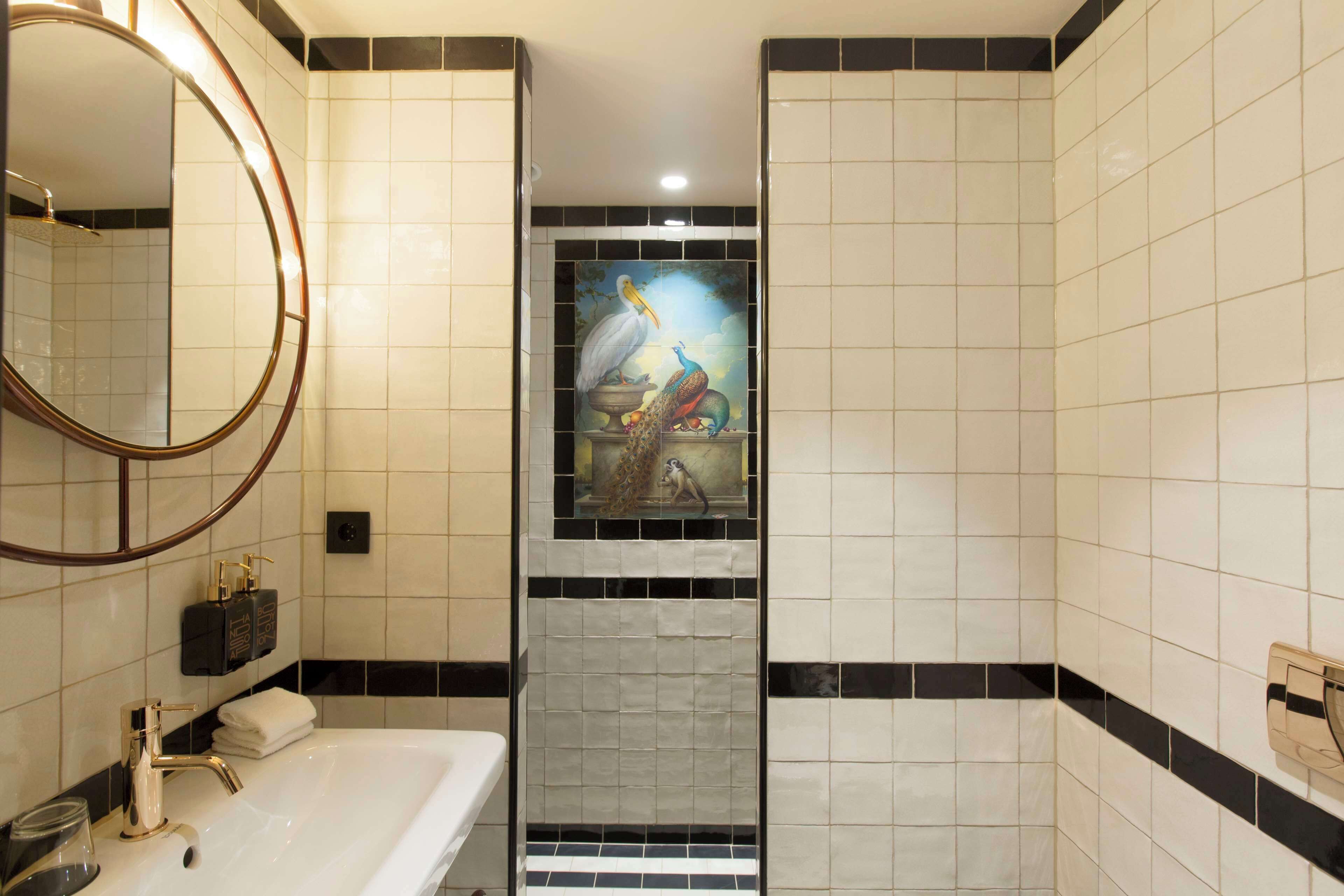 A bathroom with a white sink, a round mirror, and a decorative tile mural featuring birds.