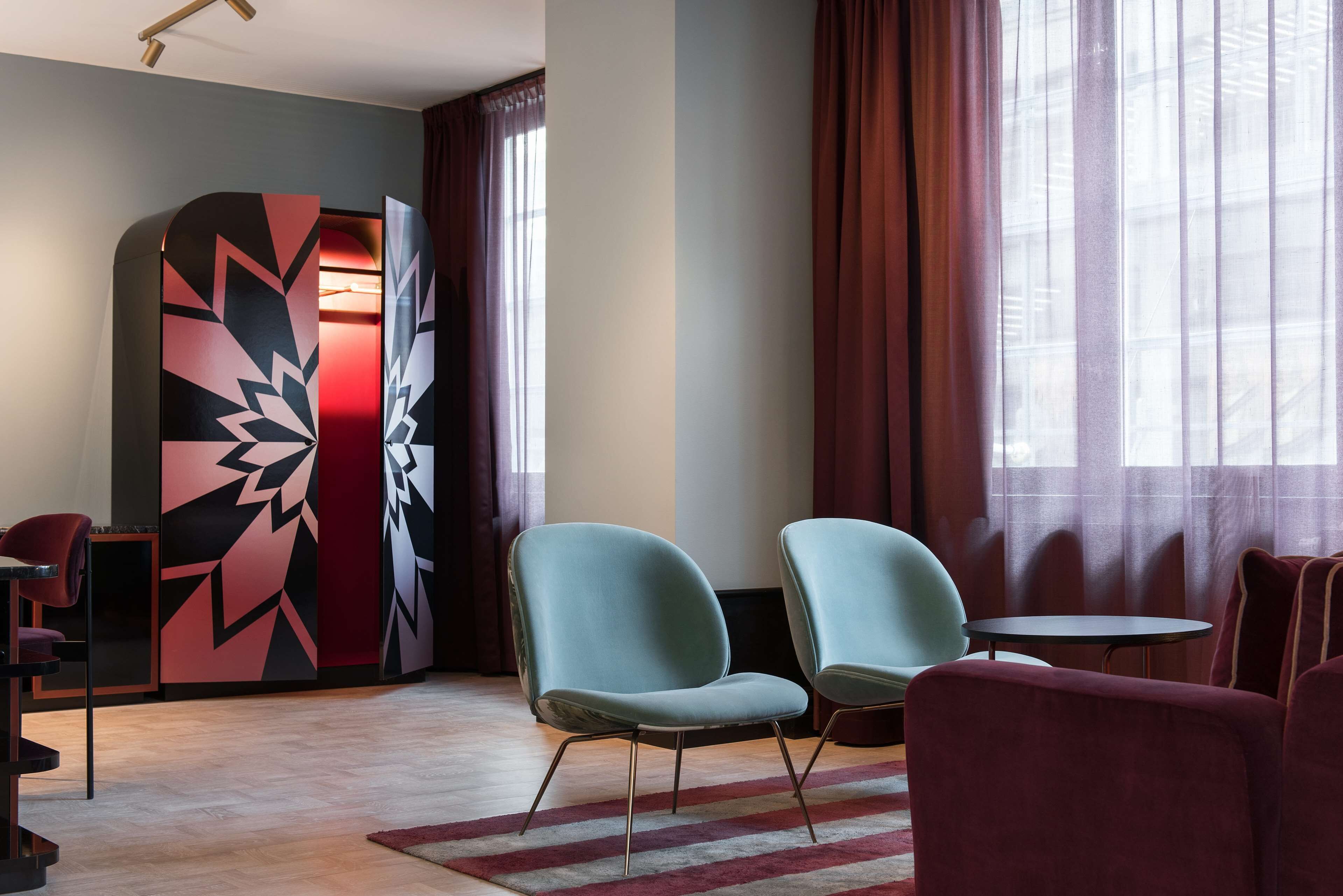 Una habitación moderna con dos sillas azul claro, una pequeña mesa redonda y un armario con estampado rojo y negro.