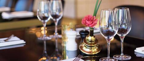 Un ambiente de restaurante con una mesa lista para comer, con copas de vino, un florero con una flor y una vela.