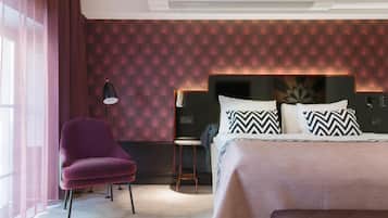 Ett modernt hotellrum med en stor säng, en stol, en liten pall och ett stort fönster med tunna, genomskinliga gardiner.