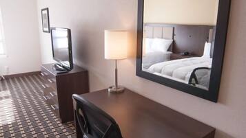 Habitación de hotel con escritorio, silla, lámpara y un espejo grande que refleja la cama.