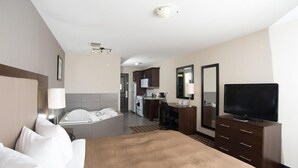 Habitación de hotel con cama, escritorio, televisor y baño visible a través de una puerta abierta.