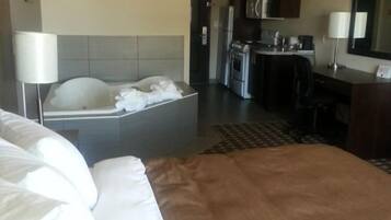 Una habitación de hotel con una cama grande, un área de descanso pequeña, una kitchenette y un baño.