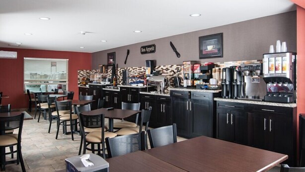 Un restaurante con mesas y sillas de madera oscura, una barra de café con varias máquinas de café y un salpicadero de azulejos.