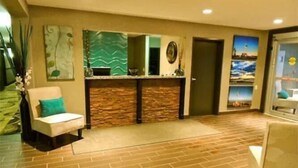 A reception area with a stone counter, a reception desk, a chair with a teal cushion, and a wall with a landscape painting. - Carlyle Western Star Inn & Suites (Carlyle)