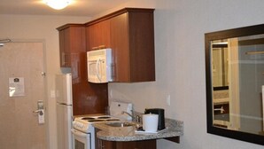 A compact kitchen with wooden cabinets, a built-in microwave, a stove, and a sink. - Carlyle Western Star Inn & Suites (Carlyle)