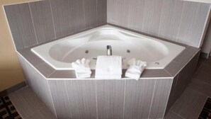 A corner bathtub with a modern design, a built-in seat, and a towel rack with towels. - Carlyle Western Star Inn & Suites (Carlyle)