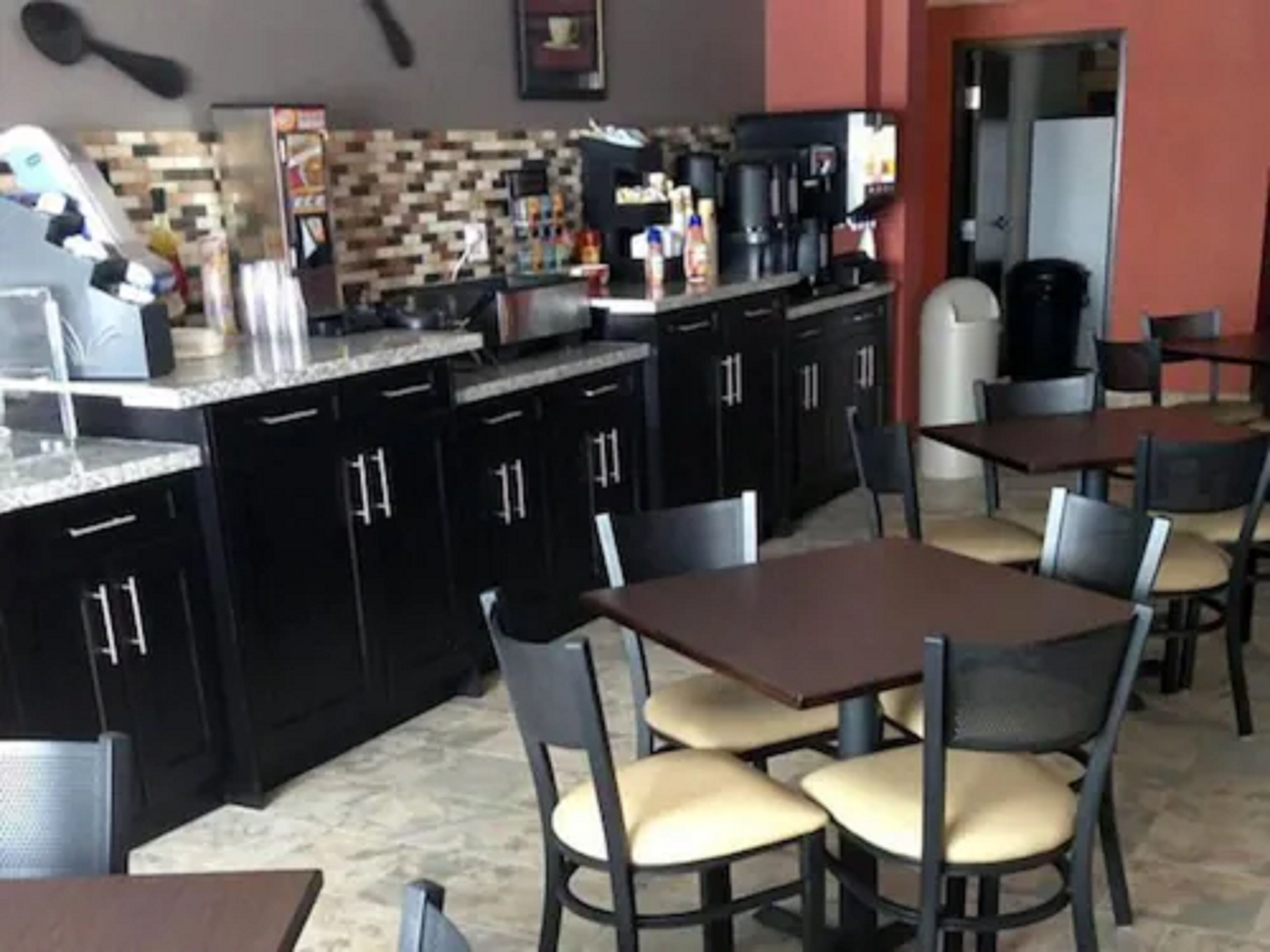 Un restaurante con armarios negros, salpicadero de azulejos y varias mesas y sillas.
