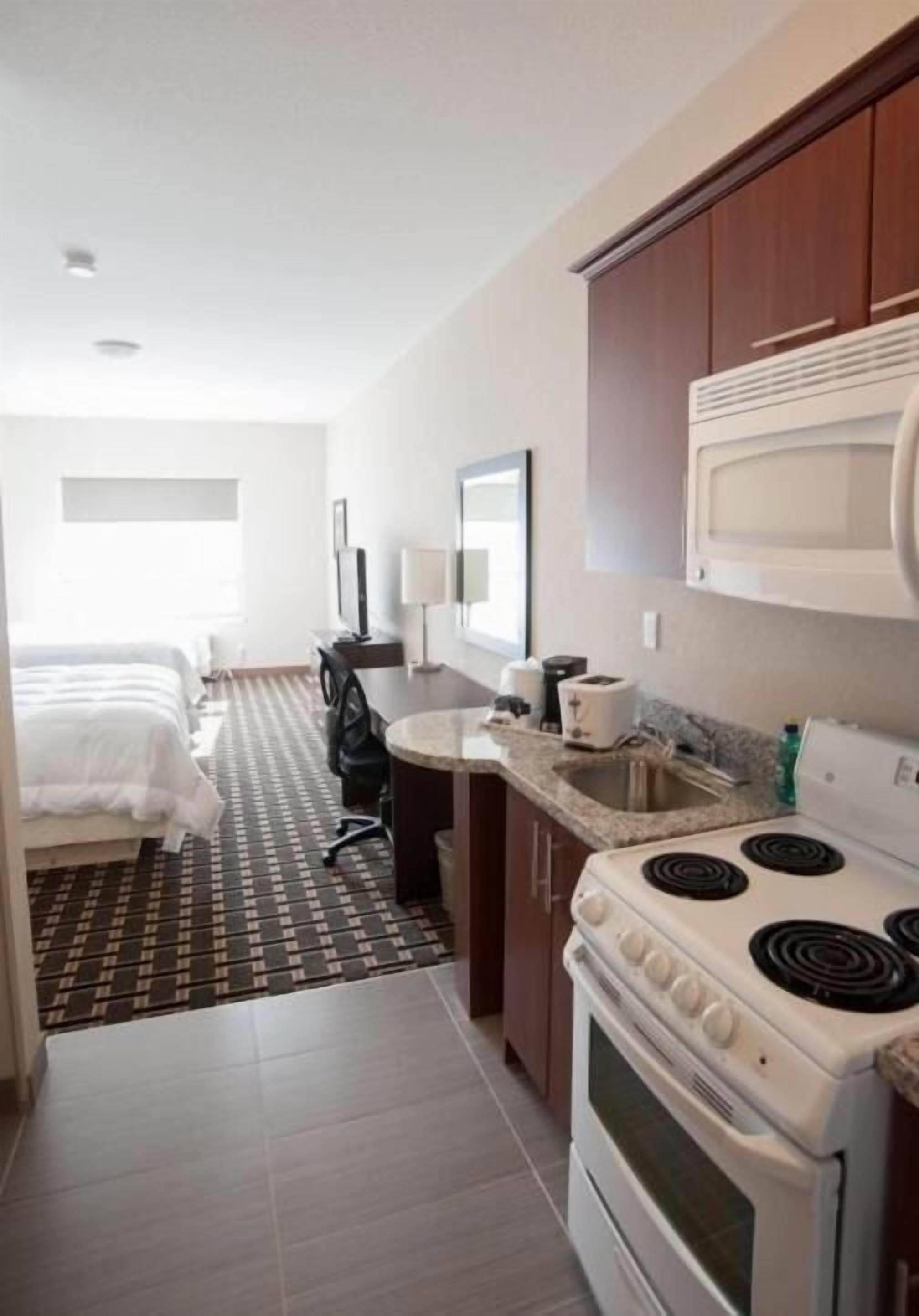 A compact hotel room with a kitchenette, a bed, a desk, and a television.