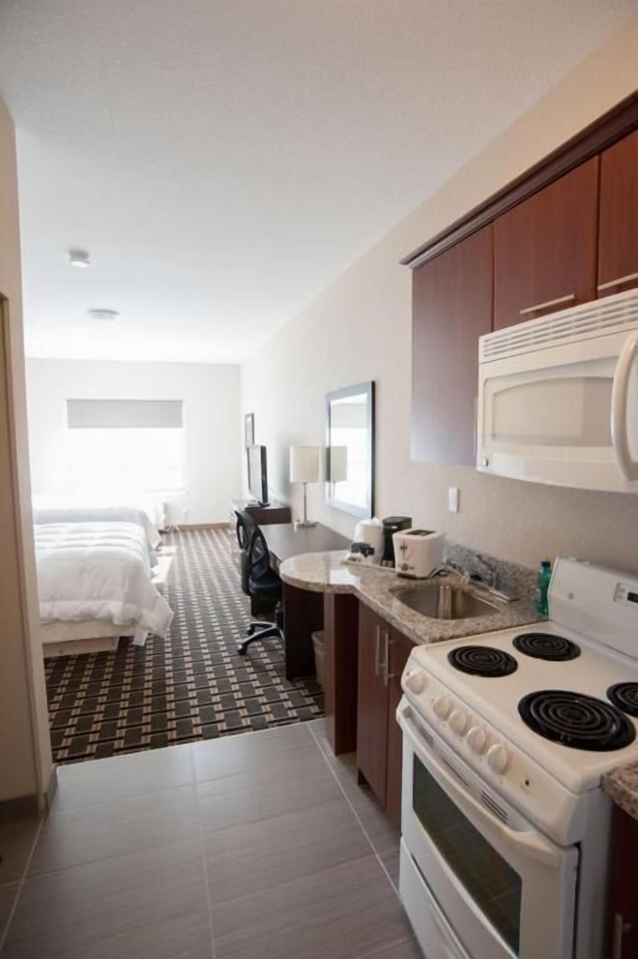 Una habitación de hotel compacta con kitchenette, cama, escritorio y televisión.