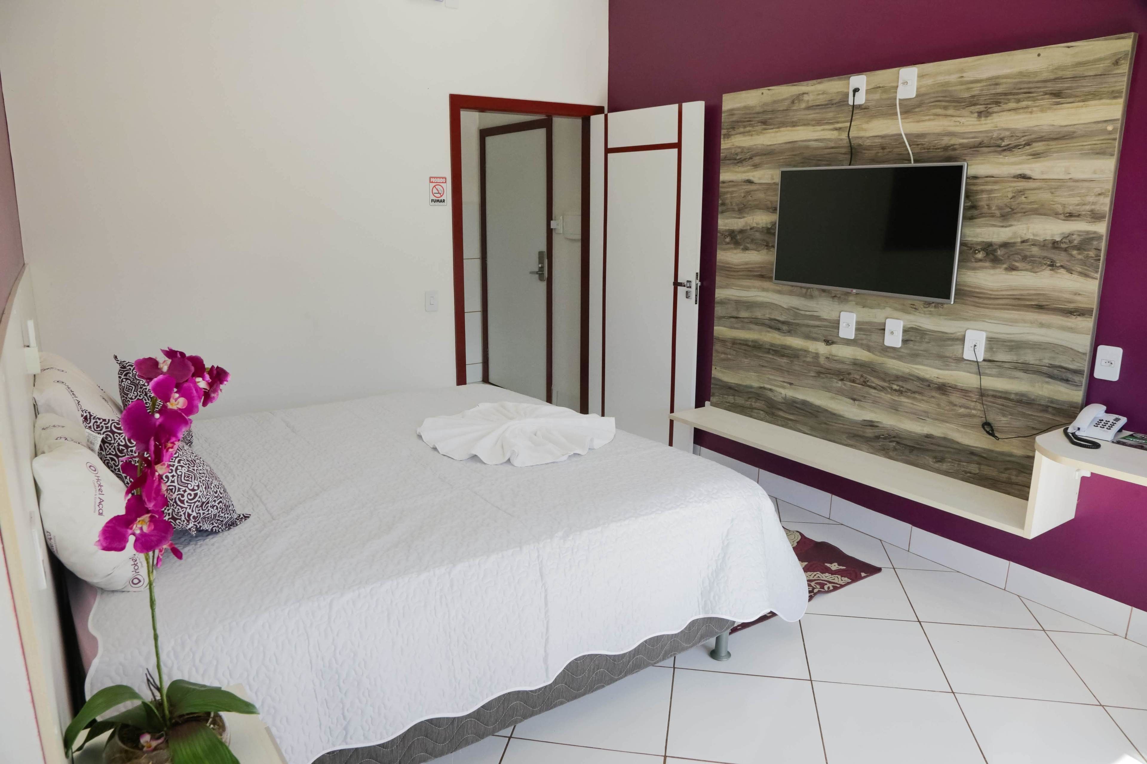 Ein Schlafzimmer mit einem Bett, einem an einer Holzvertäfelung angebrachten Fernseher, einem Nachttisch mit Telefon und einer Tür zu einem weiteren Raum.