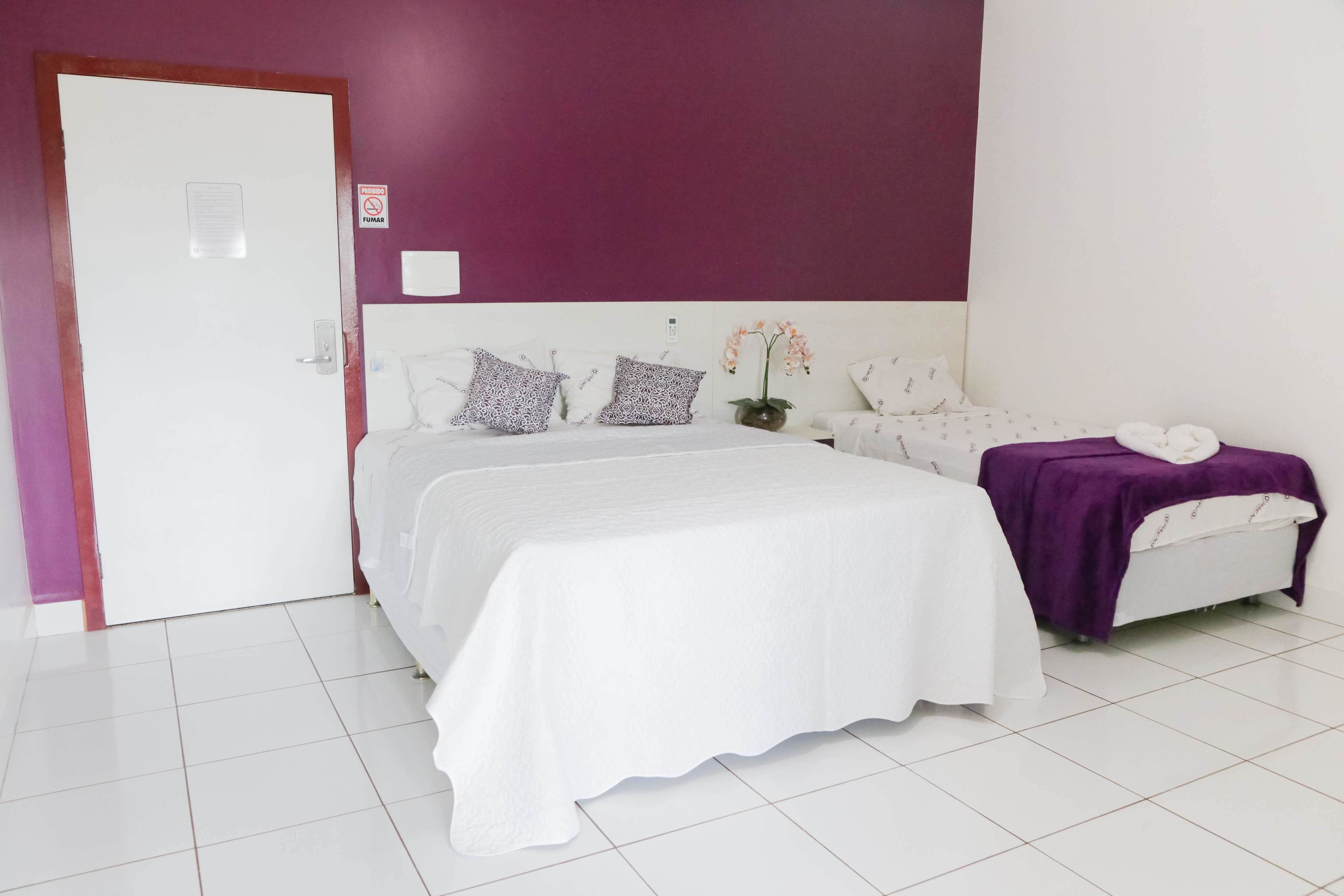 A bedroom with a white bed, purple walls, and a white door.