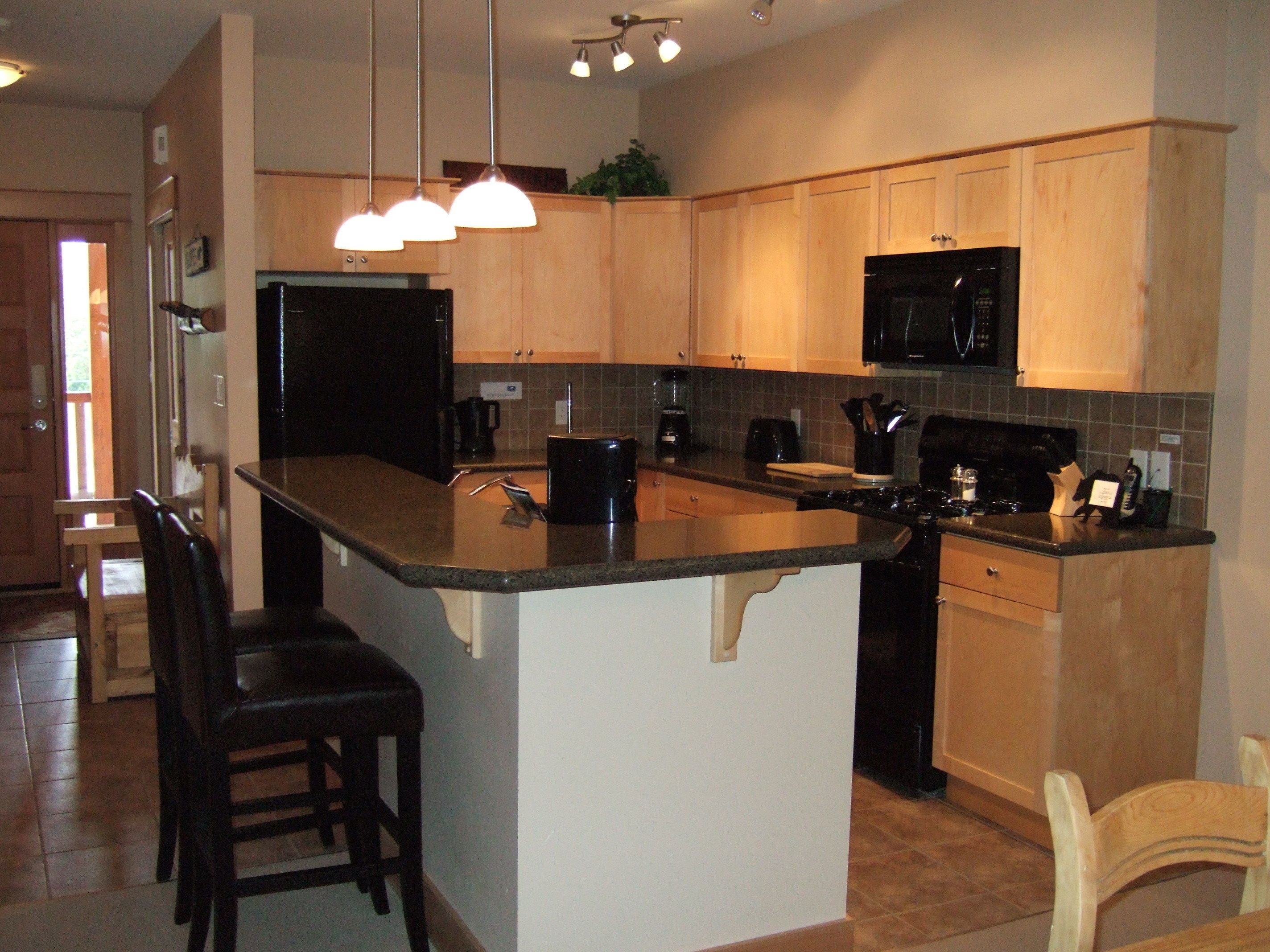 A modern kitchen with wooden cabinets, a black refrigerator, a microwave, and a large island with bar stools.