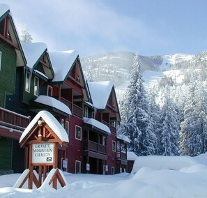 Un alojamiento de varios pisos con un letrero que dice Granite Mountain Chalets, rodeado de árboles y montañas cubiertas de nieve.