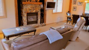 A cozy living room with a stone fireplace, a flat-screen TV mounted on the wall, and comfortable seating. - Red Mountain Village Condos (Rossland)