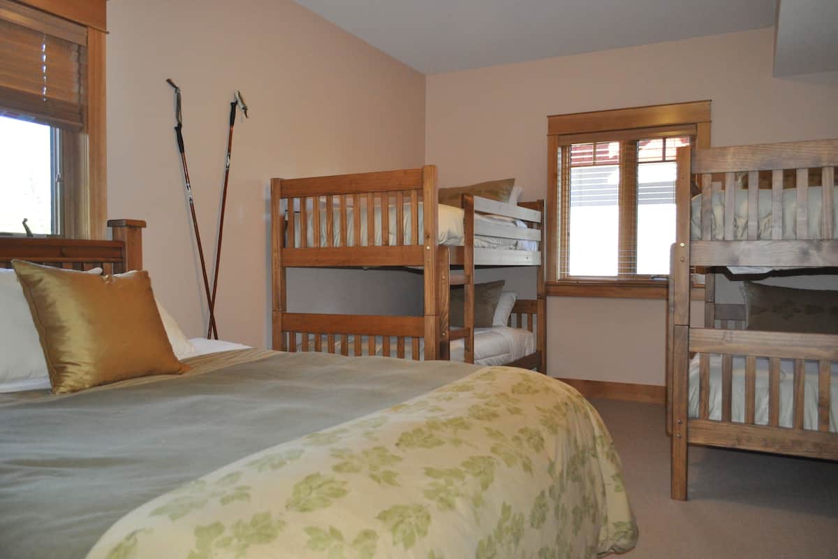 A bedroom with a large bed, two bunk beds, wooden headboards, and a window with blinds.