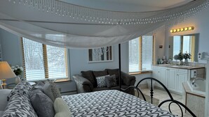 Une chambre à coucher avec une couvre-lit à motifs, une table de chevet avec une lampe, une chaise, une commode et une coiffeuse avec un miroir et un lavabo.