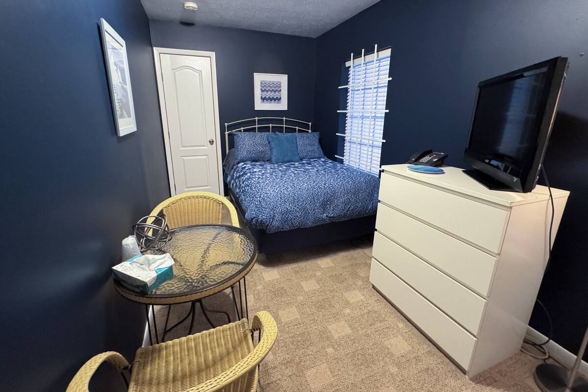 Une chambre à coucher comprenant un lit, une télévision, une commode, une chaise et une petite table.